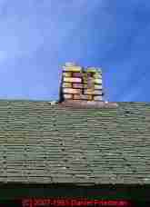 Photograph of a brick chimney missing bricks, no cap.