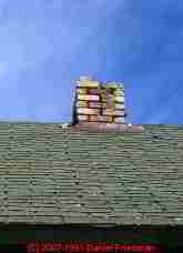 Photograph of a brick chimney missing bricks, no cap.