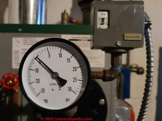 Residential steam boiler pressure gauge showing that the pressure is close to zero; above and to the right of the pressure gauge we see the steam boiler pressure control (C) Daniel Friedman at InspectApedia.com 