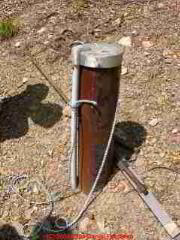 Photograph of  a modern steel well casing and cap extending properly above grade level and properly capped. You can see from
the gray plastic conduit that electrical wires enter the well, informing you that this well is served by an in-well submersible well pump.