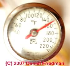 Photograph of a dial thermometer reading a high output temperature at an air conditioning compressor