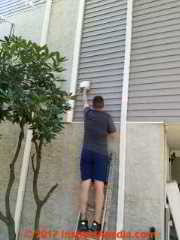 Brian Gilligan cleaning lint from the exhaust of a second-floor clothes dryer wall vent - avoid this fire hazard by regular cleaning. (C) InspectApedia.com D Friedman B Gilligan